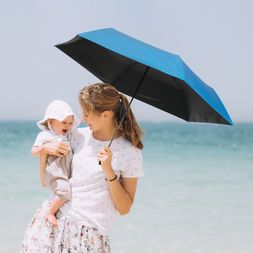 Am Strand hält eine Frau mit Baby im Arm einen blauen Knirps HeatShield Regenschirm, der zuverlässigen UV-Schutz und Hitzere­duzierung bietet